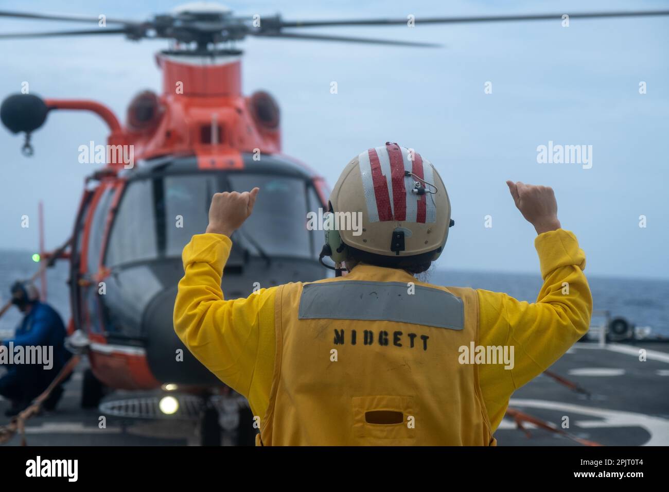 L'officier du signal d'atterrissage sur le navire de la Garde côtière Midgett (WMSL 757) donne des directives à l'équipage d'un hélicoptère Dolphin de Barbers point MH-65 tout en effectuant des opérations d'arrimage d'hélicoptère au large d'Oahu, Hawaï, 21 février 2023. Les équipages sont formés pour embarquer et faire le plein d'hélicoptères pendant que le dispositif de coupe est en marche dans diverses conditions météorologiques. (Photo de la Garde côtière par l'officier Petty 3rd classe Briana carter) Banque D'Images