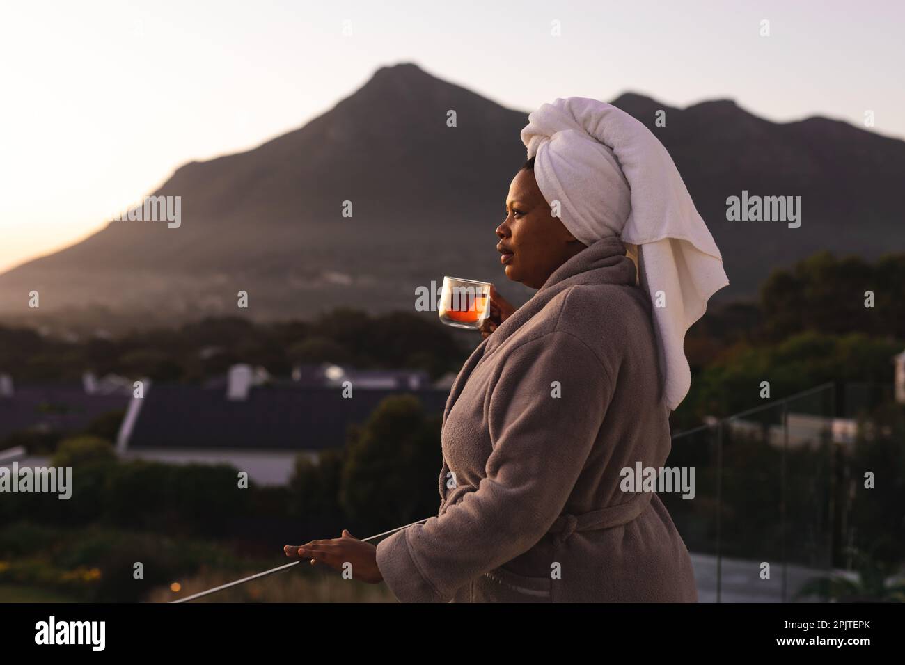 Femme afro-américaine de bonne taille, portant un peignoir et une serviette sur la tête, buvant du thé sur le balcon Banque D'Images