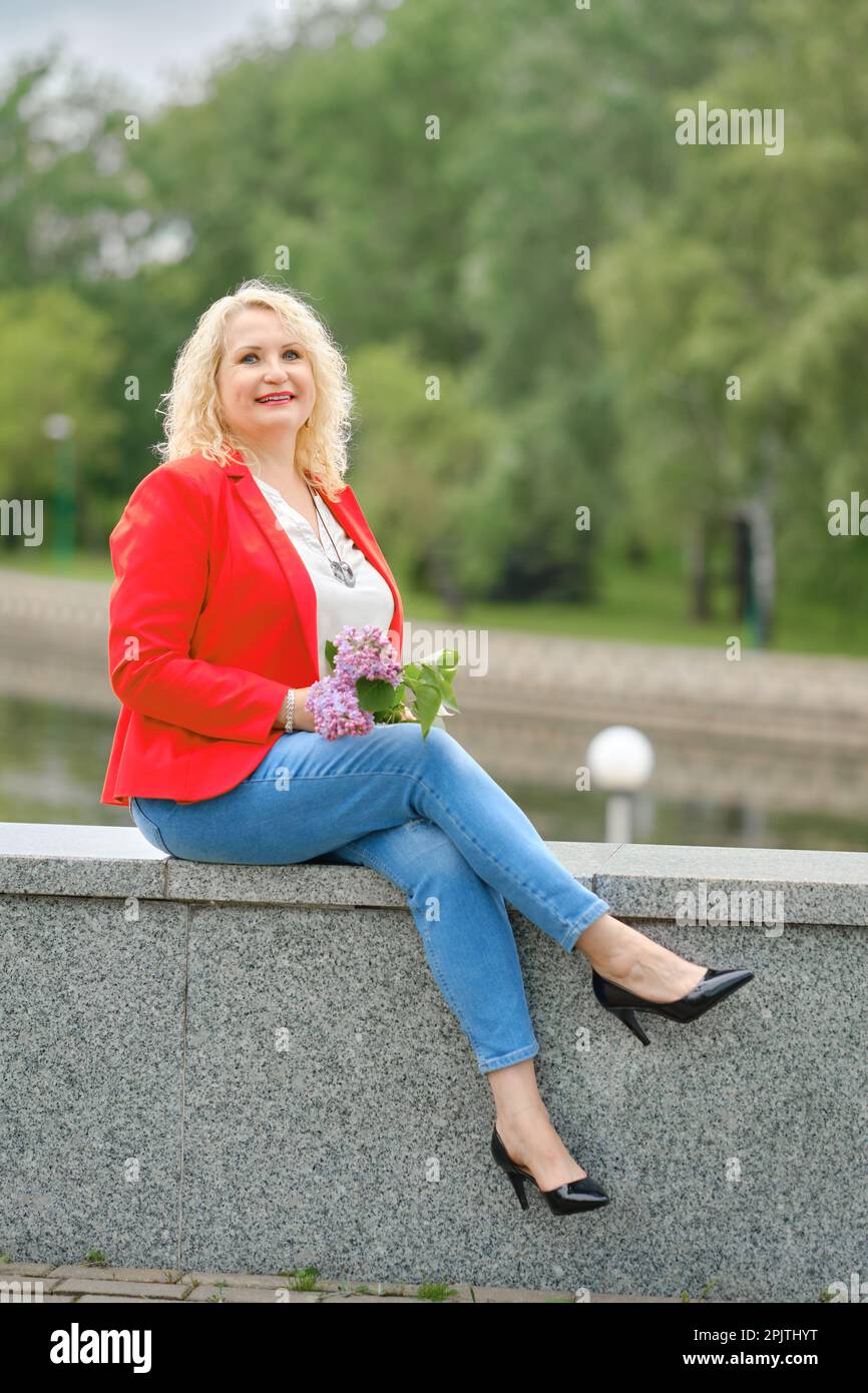 Une heureuse femme d'âge moyen est assise sur le remblai dans un parc de la ville Banque D'Images