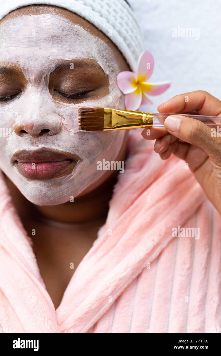 Femme afro-américaine décontractée de grande taille ayant un masque de beauté appliqué au visage au spa Banque D'Images