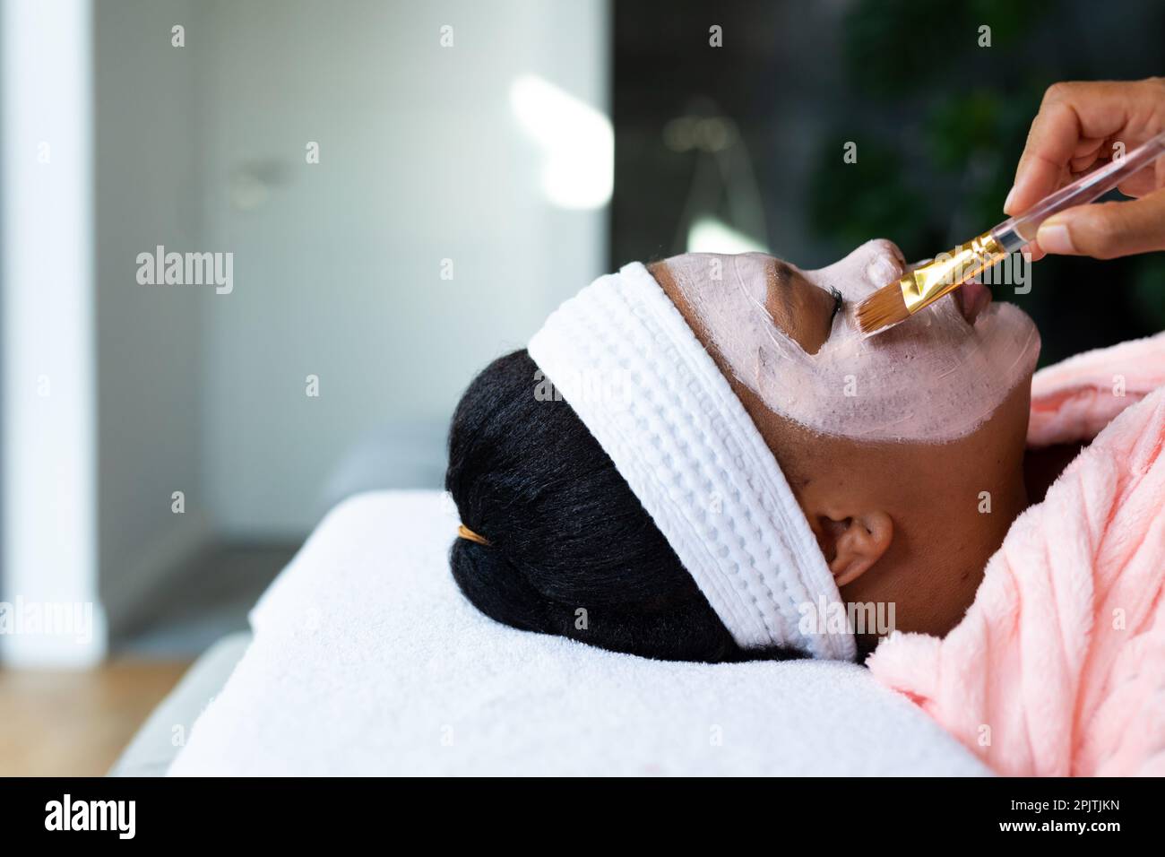 Femme afro-américaine décontractée de plus grande taille ayant un masque de beauté appliqué sur le visage au spa, copier l'espace Banque D'Images