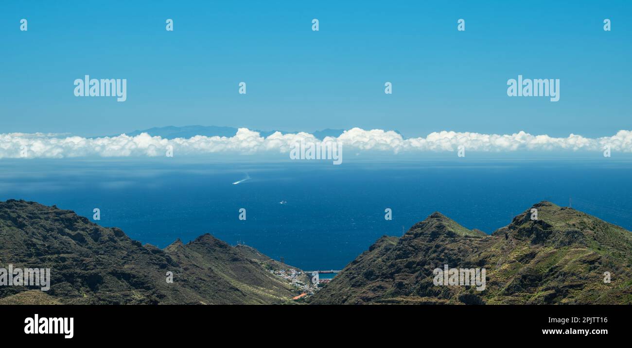 Longue bande étroite de nuages comme une ligne entre le ciel et l'océan. Image panoramique. Paysage rocheux au premier plan. Banque D'Images