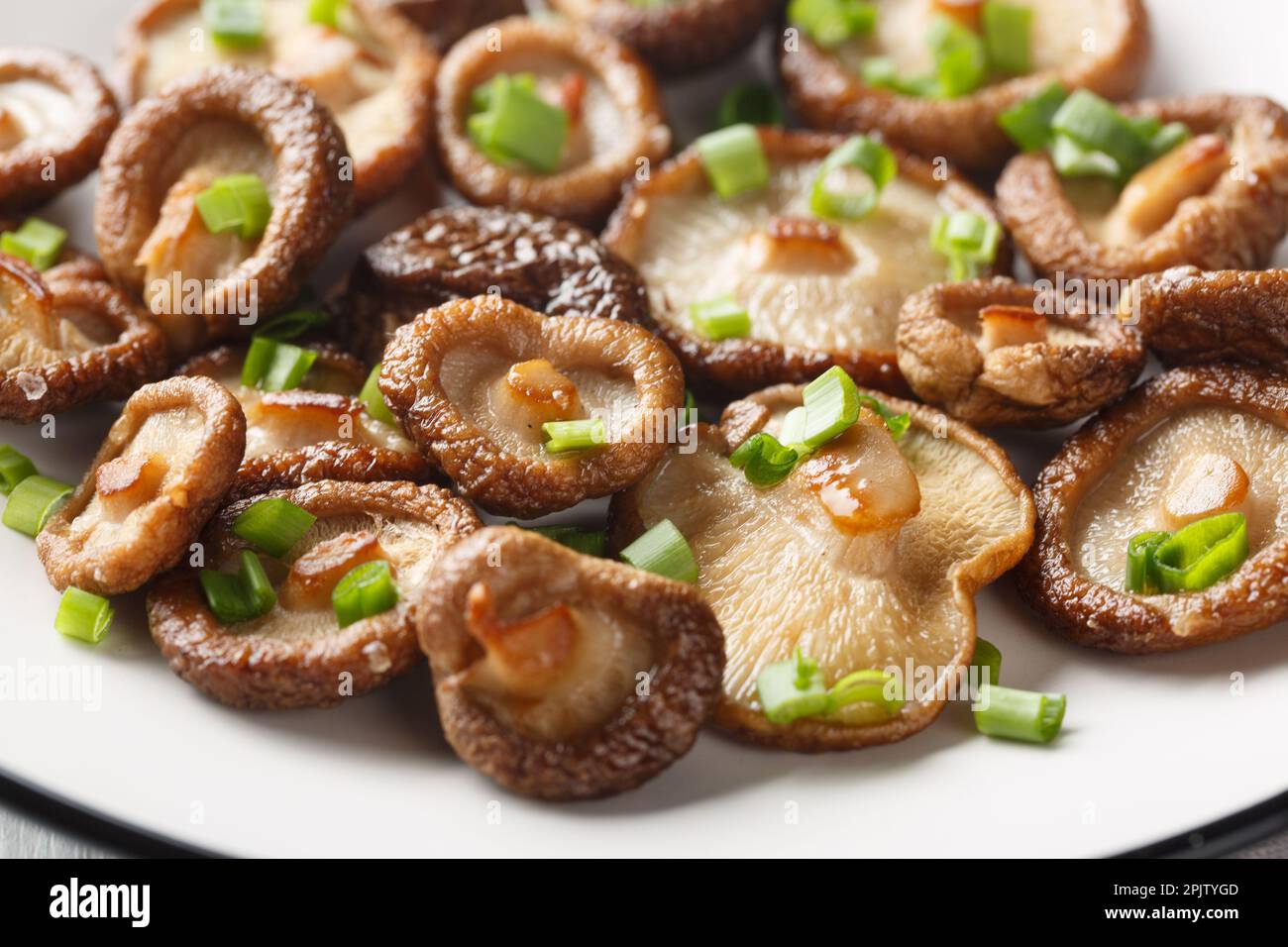 Champignons shiitake frits faits maison avec oignons verts en gros plan sur une assiette blanche. Horizontale Banque D'Images