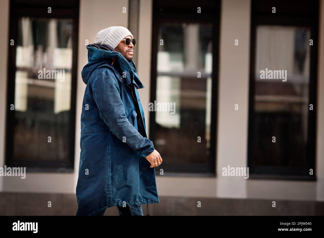 Portrait d'un beau homme afro-américain marchant en ville, portant un parka élégant, un chapeau tricoté et des lunettes de soleil. Street style mode homme Mo Banque D'Images
