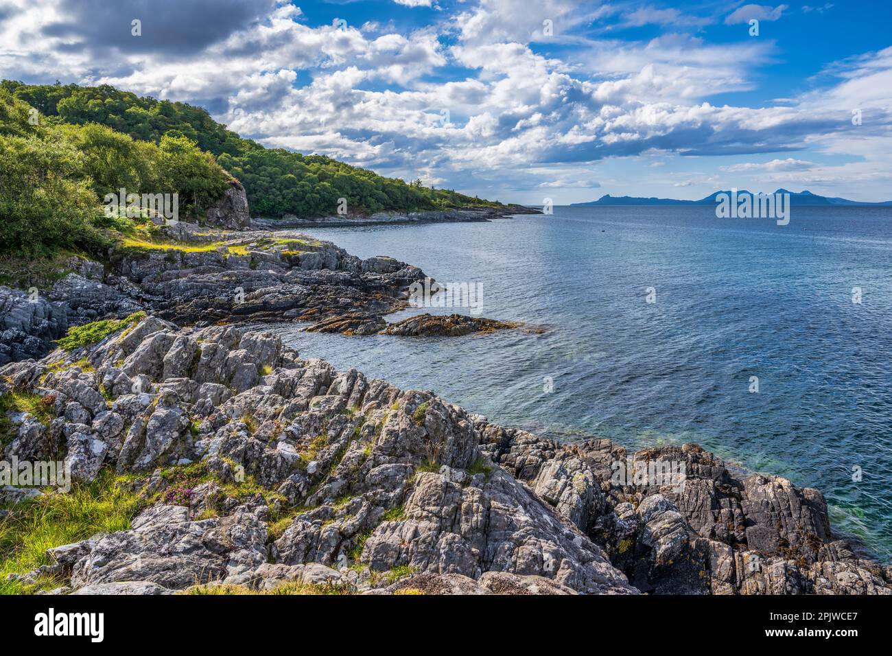 Littoral rocheux sur la baie de Samalaman, avec l'île d'Eigg et les montagnes de Rum à distance, à Glenuig sur la péninsule Ardnamurchan à Lochaber, en Écosse Banque D'Images