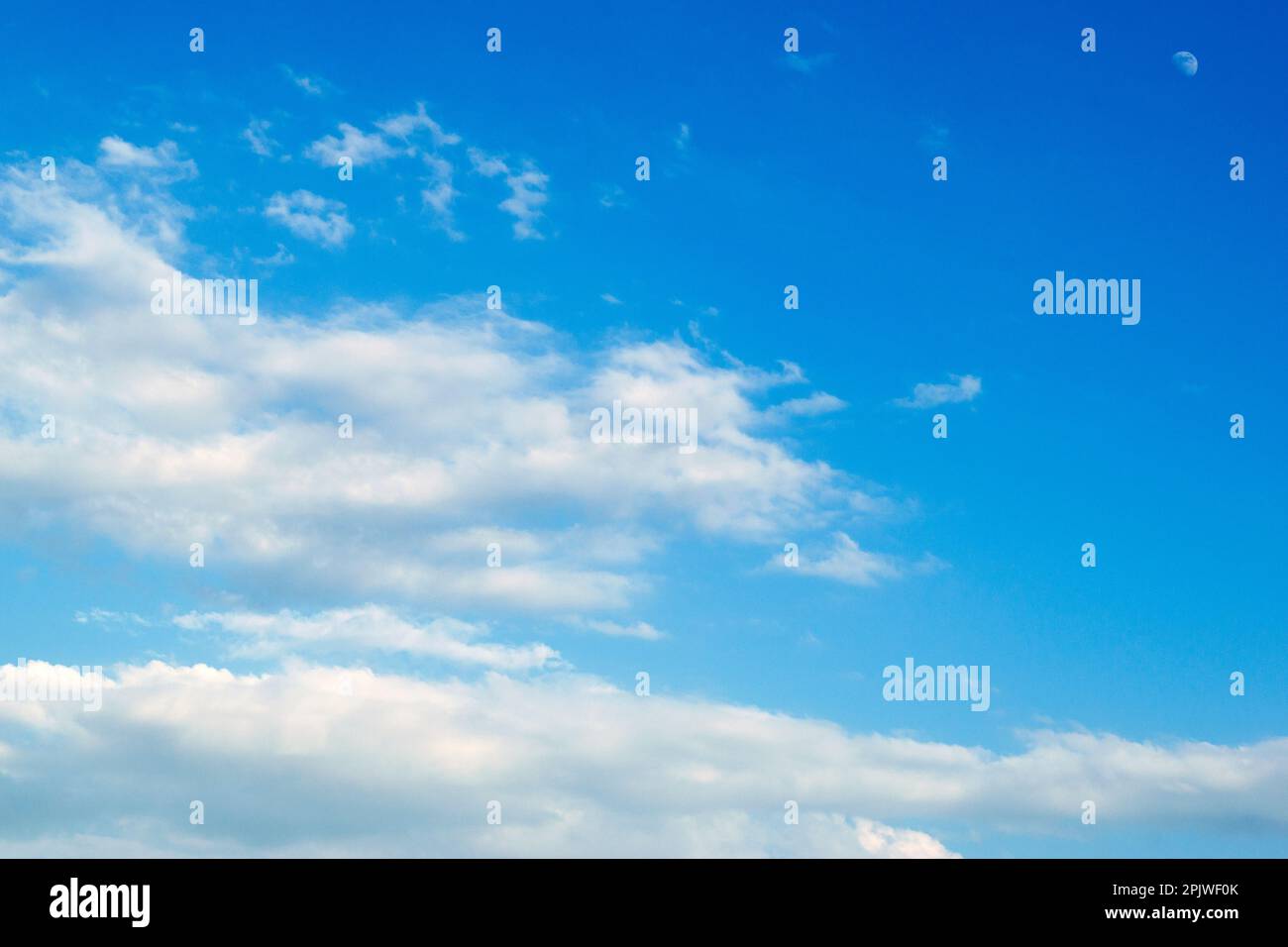 Beau ciel bleu avec lune visible et quelques nuages blancs inoffensifs et estivaux. Banque D'Images