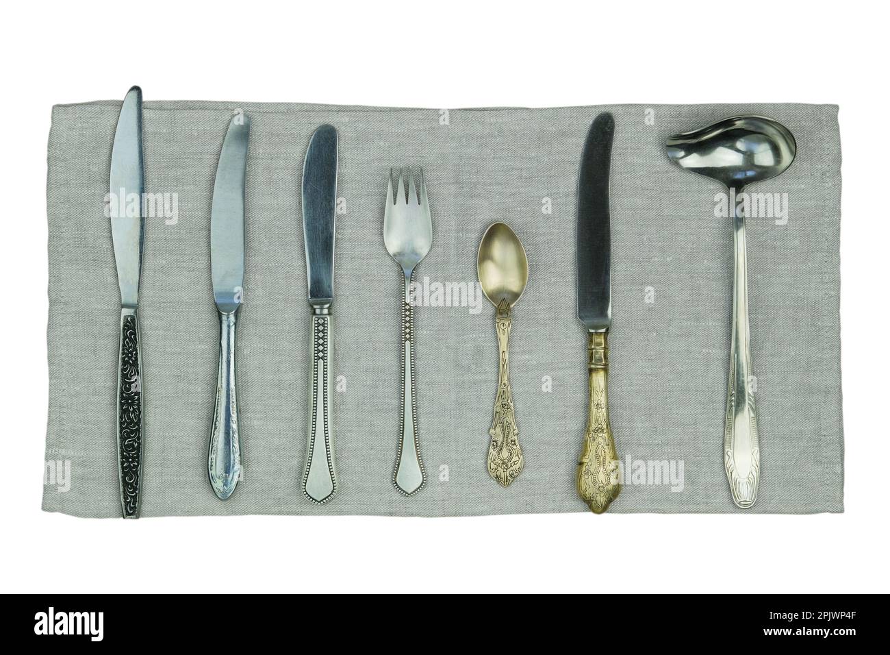 Variété de couteaux, fourchettes et autres ustensiles de cuisine sur une serviette en lin isolée sur un fond blanc. Vue de dessus. Banque D'Images