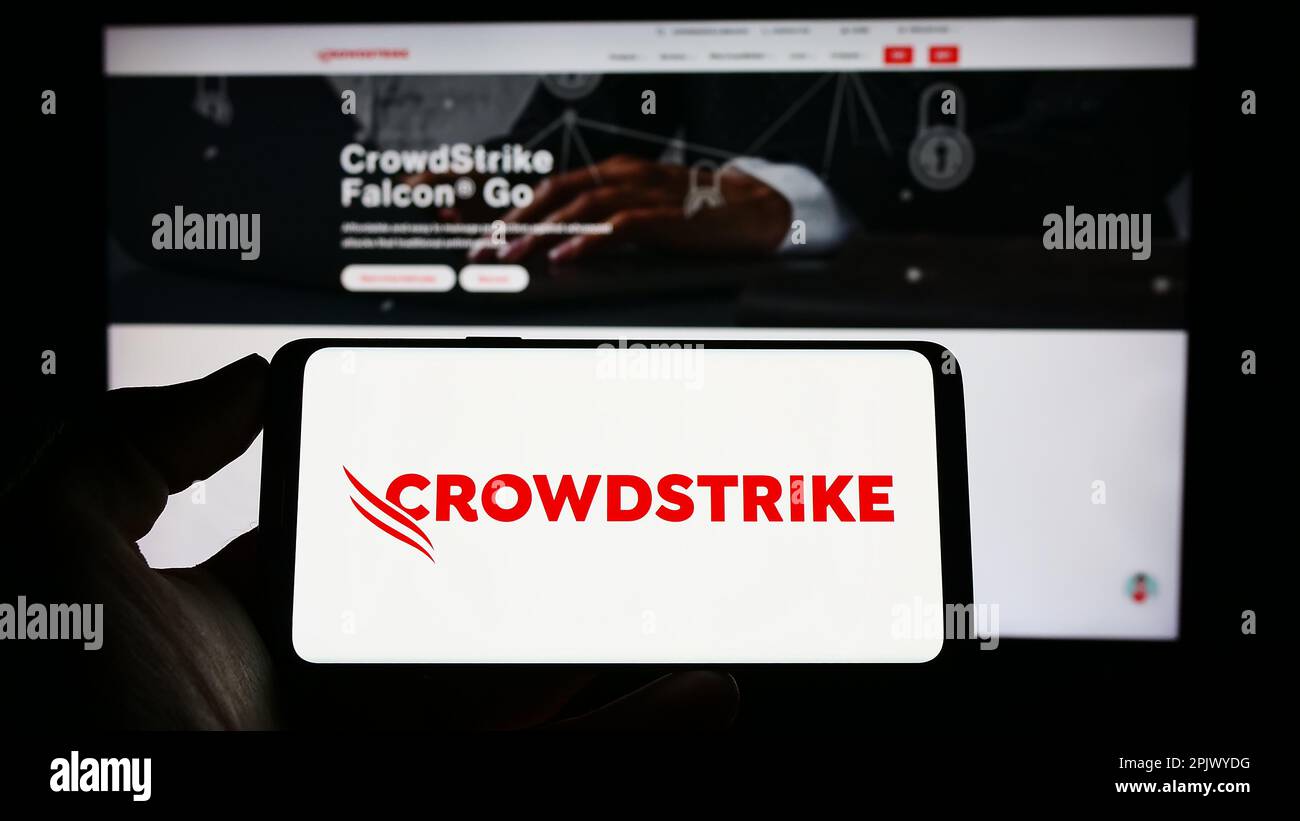 Personne tenant un téléphone cellulaire avec le logo de la société de cybersécurité CrowdStrike Holdings Inc. À l'écran devant la page Web. Mise au point sur l'affichage du téléphone. Banque D'Images