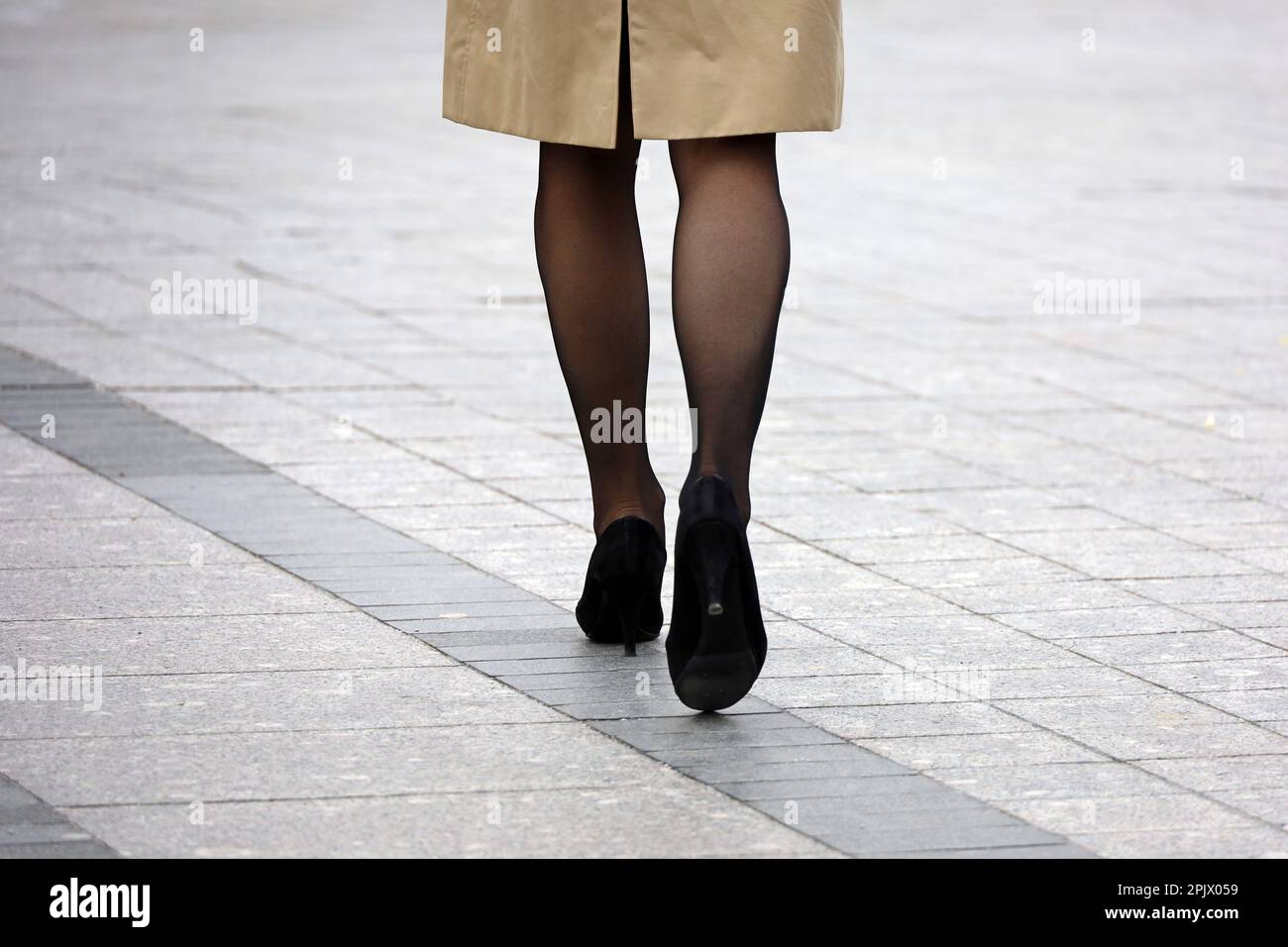 Femme mince en manteau, bas noirs et chaussures sur talons hauts marchant dans la rue, mode féminine au printemps ville Banque D'Images
