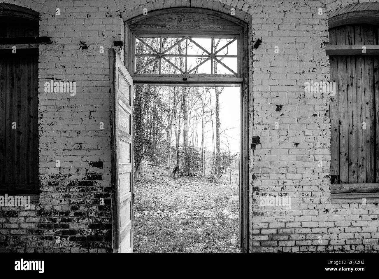 Porte en bois restaurée ouverte située entre les fenêtres avec volets et le vieux mur en briques délavées. Banque D'Images