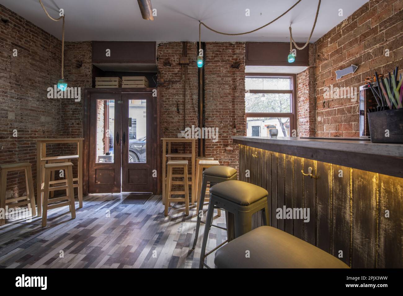 Un bar vide avec des murs en briques brutes et des tables hautes en bois blanc avec des tabourets assortis Banque D'Images