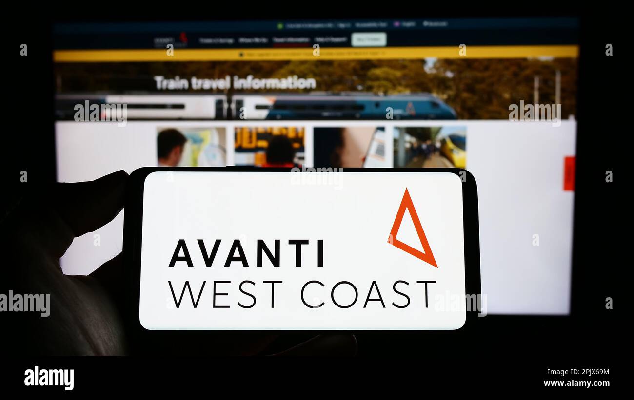 Personne tenant le téléphone portable avec le logo de la compagnie de train britannique Avanti West Coast sur l'écran en face de la page Web d'affaires. Mise au point sur l'affichage du téléphone. Banque D'Images