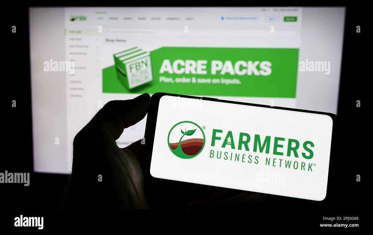 Personne tenant un téléphone portable avec logo de la plate-forme agricole Farmers Business Network (FBN) à l'écran devant la page Web. Mise au point sur l'affichage du téléphone. Banque D'Images