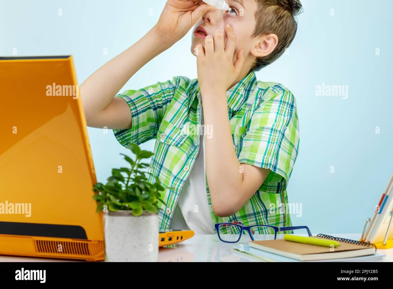 Un garçon fatigué ressent de la douleur lorsqu'il exerce ses yeux de manière excessive sur l'ordinateur, fait tomber les yeux irrités par des gouttes. Le concept de mauvaise vue chez un enfant Banque D'Images