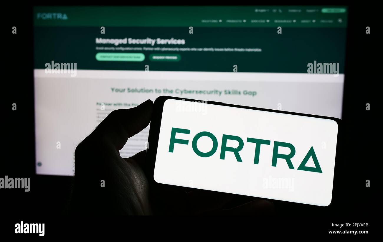 Personne tenant un smartphone avec le logo de la société américaine de cybersécurité Fortra LLC sur l'écran devant le site Web. Mise au point sur l'affichage du téléphone. Banque D'Images