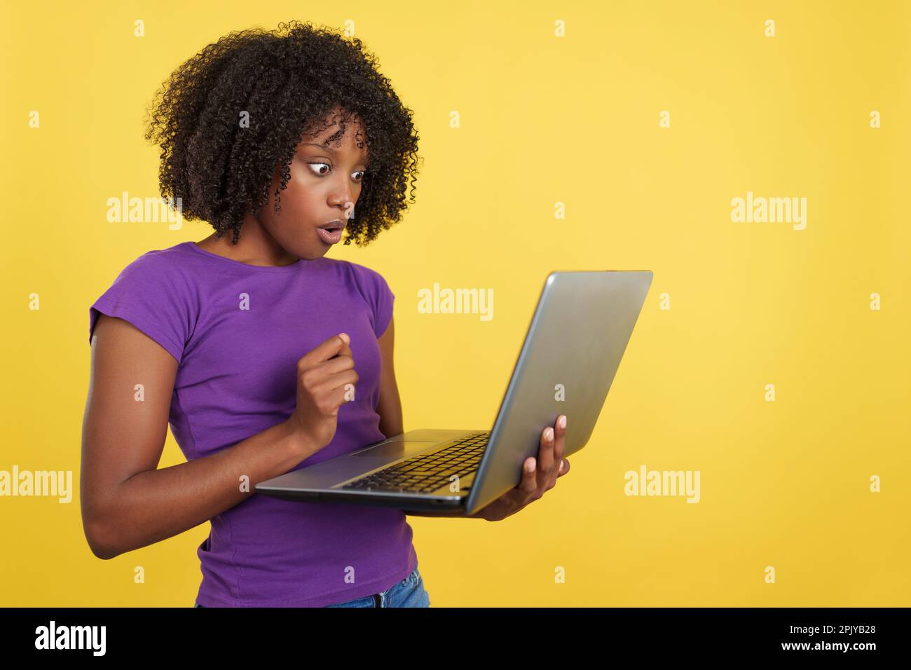 Femme aux cheveux afro à la recherche d'un ordinateur portable avec une expression choquée Banque D'Images