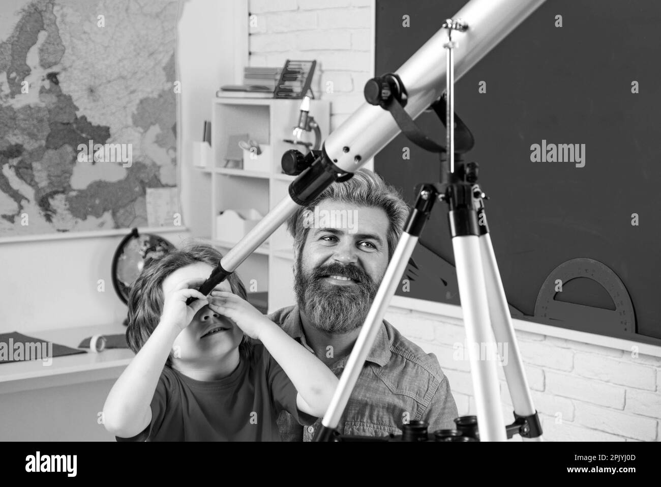 Père enseignant son à l'aide d'un télescope. Portrait de l'élève de l'école primaire étudier à l'intérieur. Fête des pères. Père et fils heureux. Banque D'Images