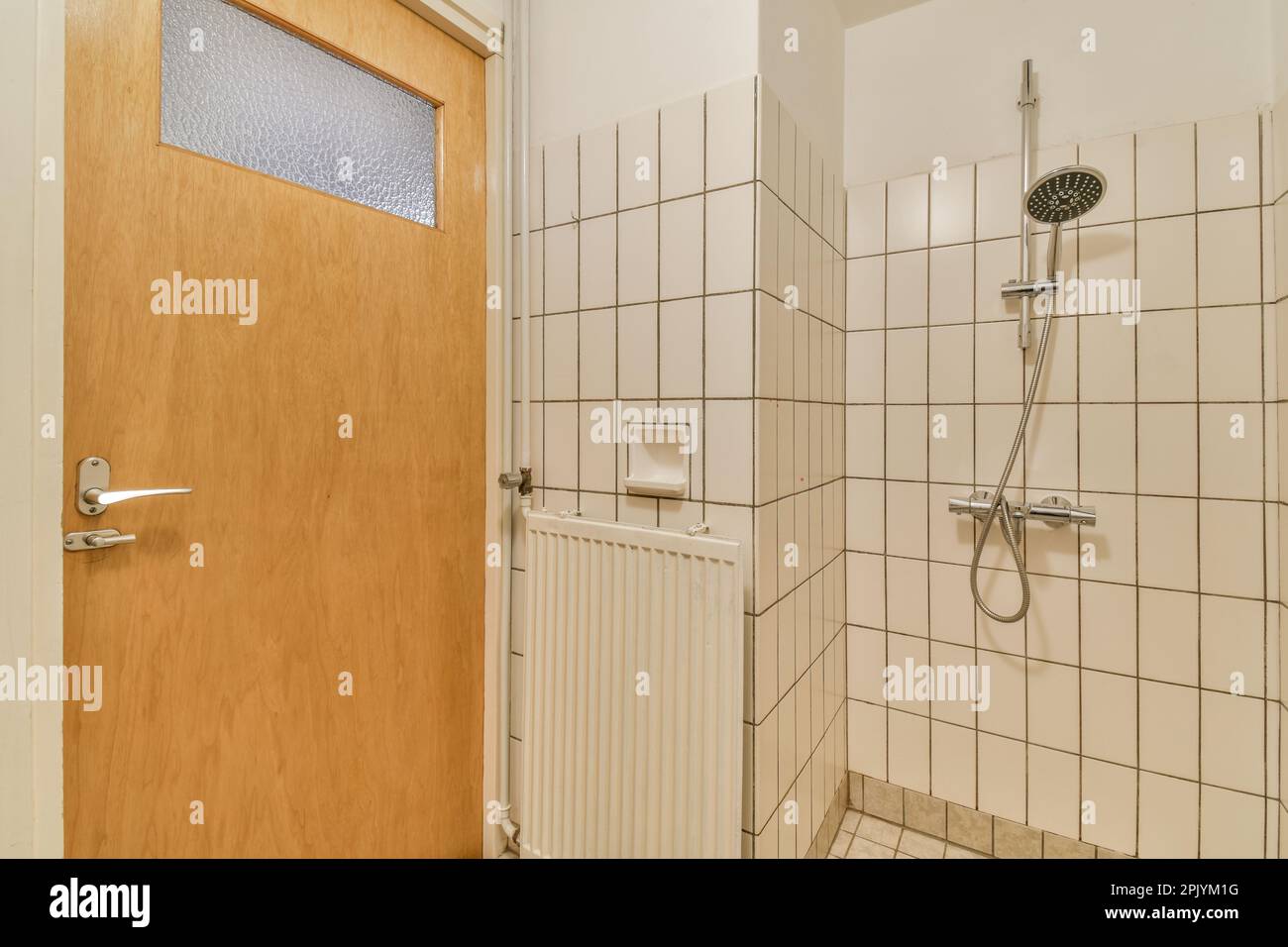 une salle de bains avec des carreaux blancs sur les murs et des lambris autour de la porte de la douche, qui est fermée pour laisser la lumière dans le Banque D'Images