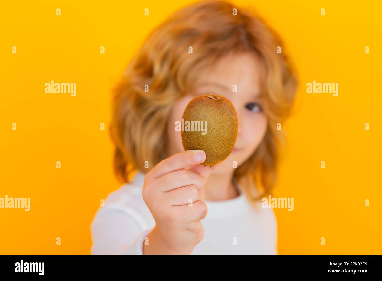 Garde d'enfants kiwi en studio. Kiwi. Studio portrait d'un petit garçon mignon avec kiwi isolé sur jaune Banque D'Images
