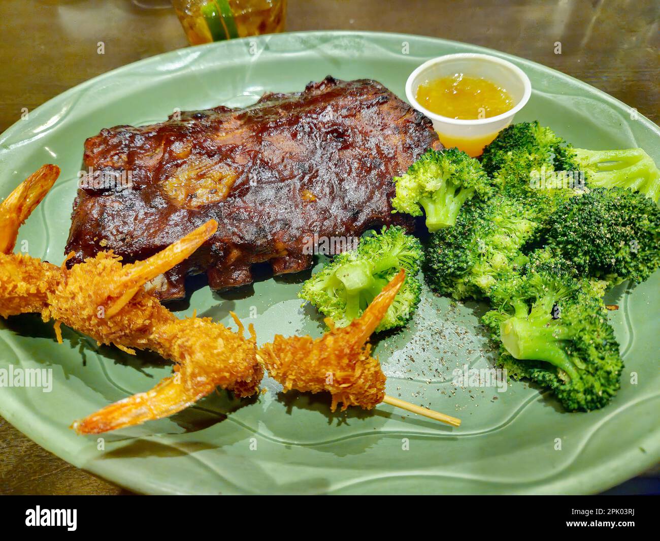 Griller les côtes de porc et les crevettes à la noix de coco avec du brocoli frais sur une assiette verte Banque D'Images