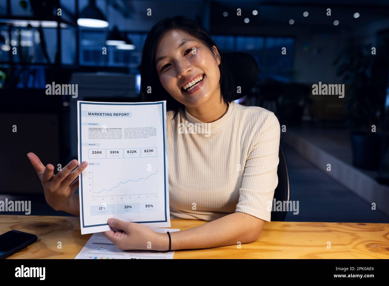 Bonne femme d'affaires asiatique tenant des documents en passant un appel vidéo, travaillant tard au bureau Banque D'Images