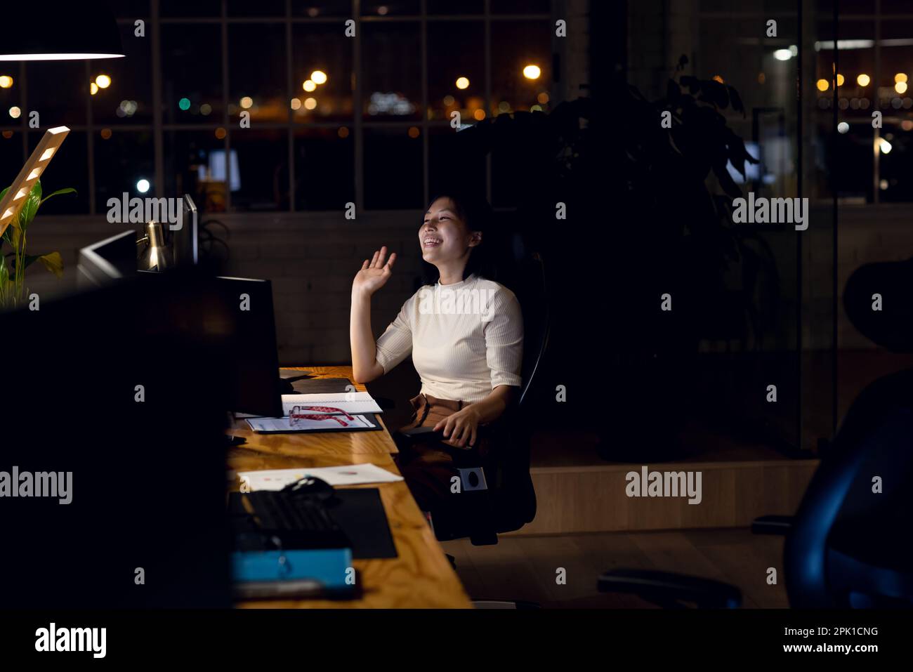 Bonne femme d'affaires asiatique assise au bureau, utilisant l'ordinateur pour les appels vidéo, travaillant tard au bureau Banque D'Images