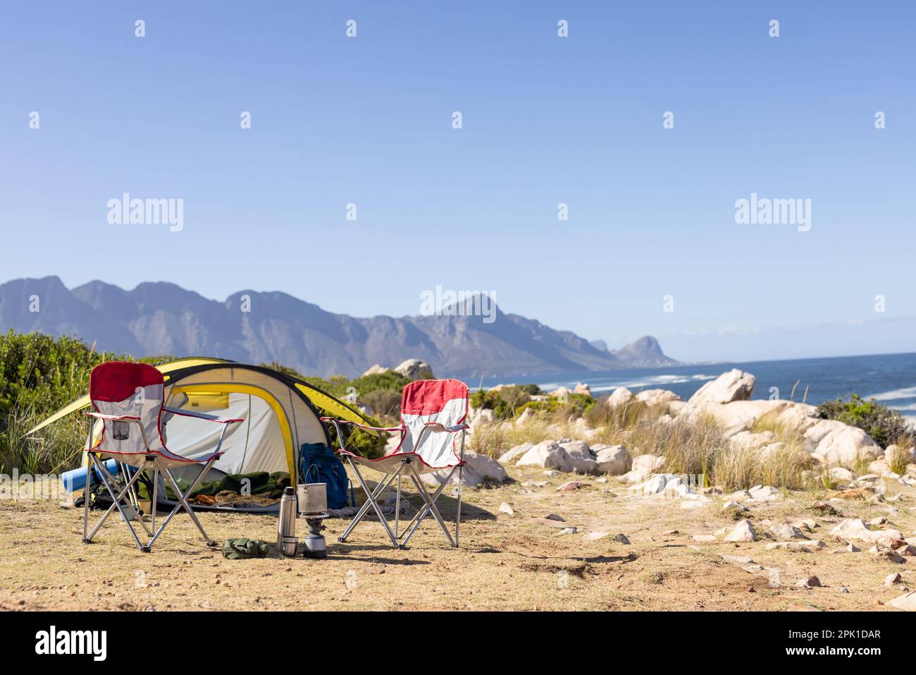 Tente jaune avec chaises de camping et équipement au-dessus des montagnes et de la mer, espace de copie Banque D'Images