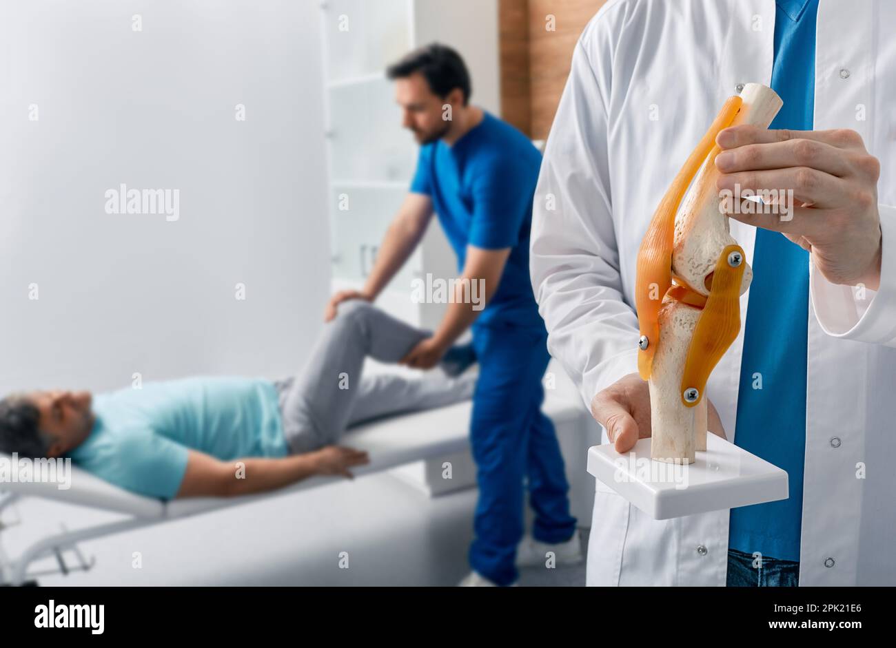 Physiothérapeute tenant le modèle anatomique de l'articulation genou-humain dans les mains, sur la séance de physiothérapie de fond pour le patient mâle. Traitements de physiothérapie a Banque D'Images