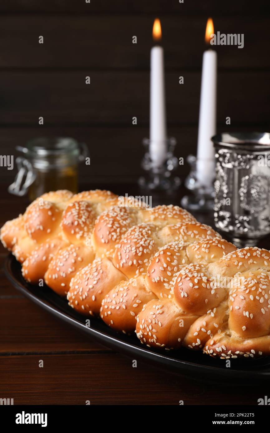 Pain tressé fait maison avec graines de sésame, gobelet et bougies sur table en bois, en gros plan. Challah traditionnel de Shabbat Banque D'Images