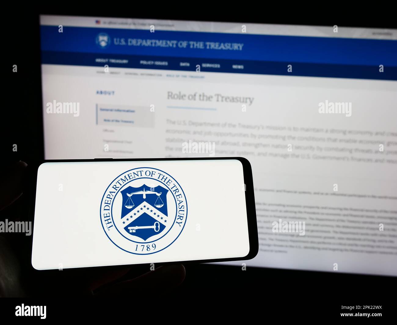 Personne tenant un smartphone avec le sceau du Département du Trésor des États-Unis (USDT) sur l'écran devant le site Web. Mise au point sur l'affichage du téléphone. Banque D'Images