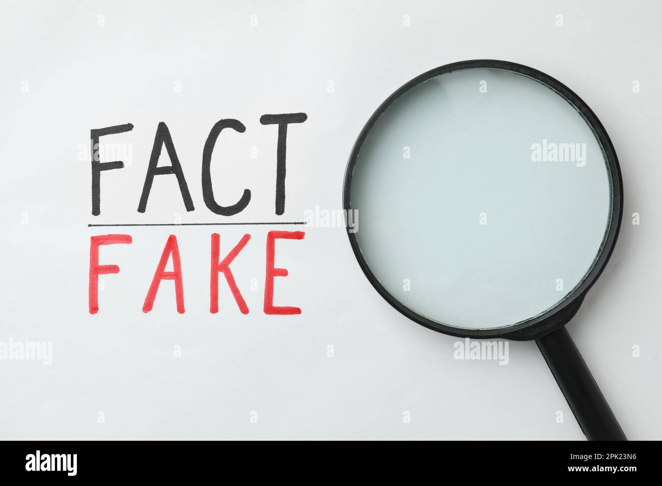 Loupe près des mots fact et fake écrit sur fond blanc, vue de dessus Banque D'Images