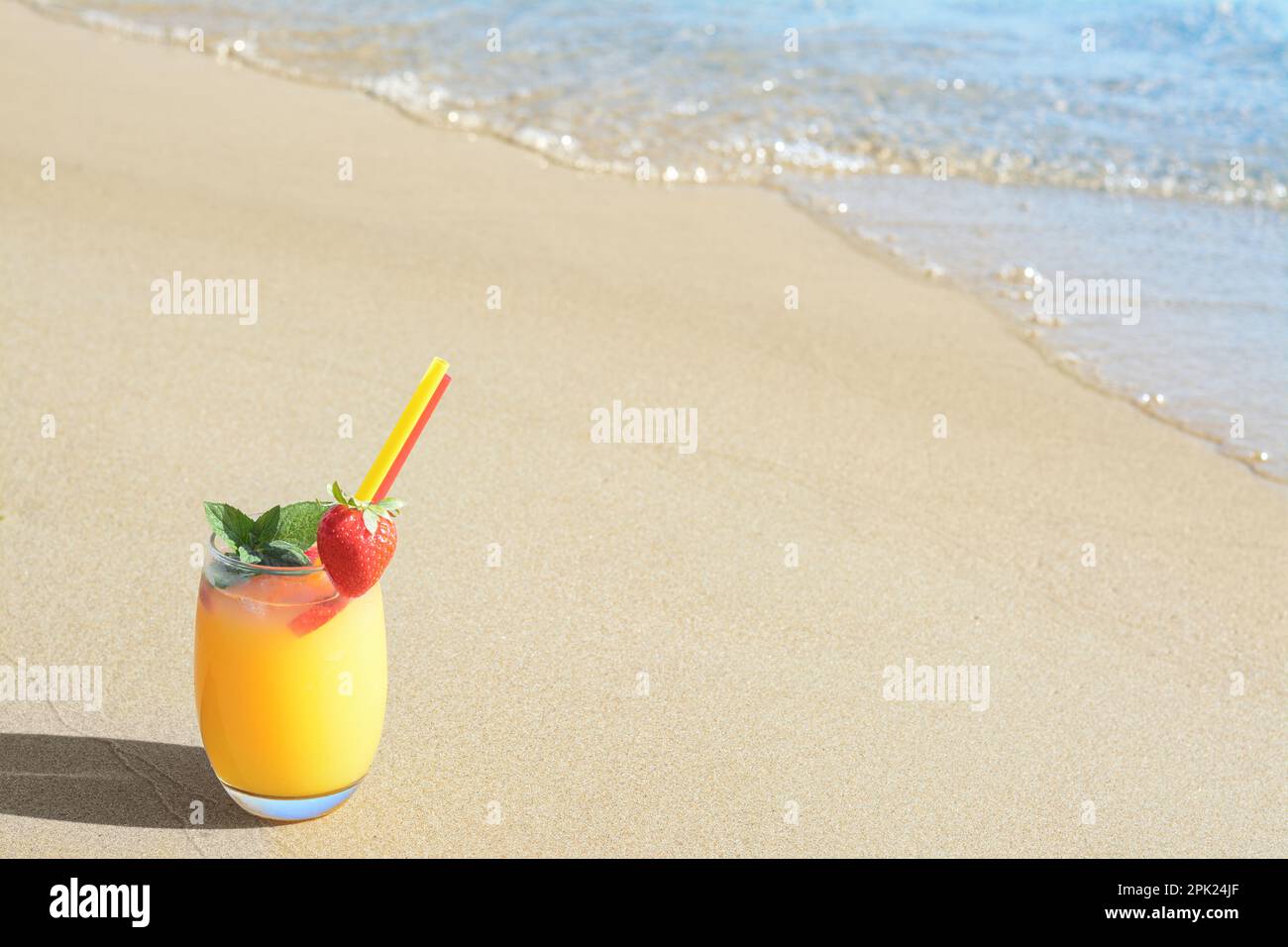 Verre de boisson rafraîchissante avec fraise sur la plage de sable près de la mer, espace pour le texte Banque D'Images