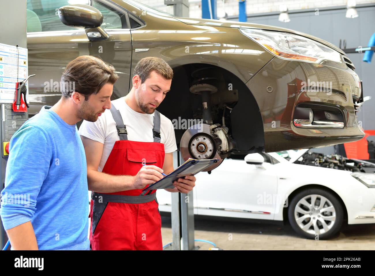 Le service après-vente dans l'atelier de réparation automobile - mécanicien et homme parler de la réparation d'un véhicule Banque D'Images