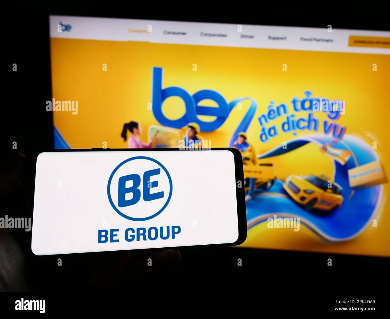 Personne tenant le téléphone portable avec le logo de la société vietnamienne de technologie être Groupe JSC sur l'écran en face de la page Web d'affaires. Mise au point sur l'affichage du téléphone. Banque D'Images