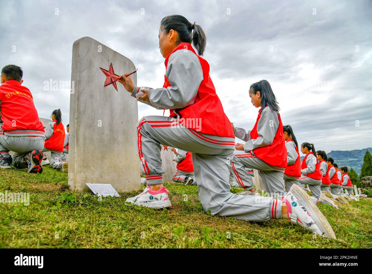 BAZHONG, CHINE - le 5 AVRIL 2023 - les élèves de l'école primaire peignent en rouge sur la pierre tombale d'un martyr inconnu au cimetière des martyrs de l'Armée rouge dans le sich Banque D'Images