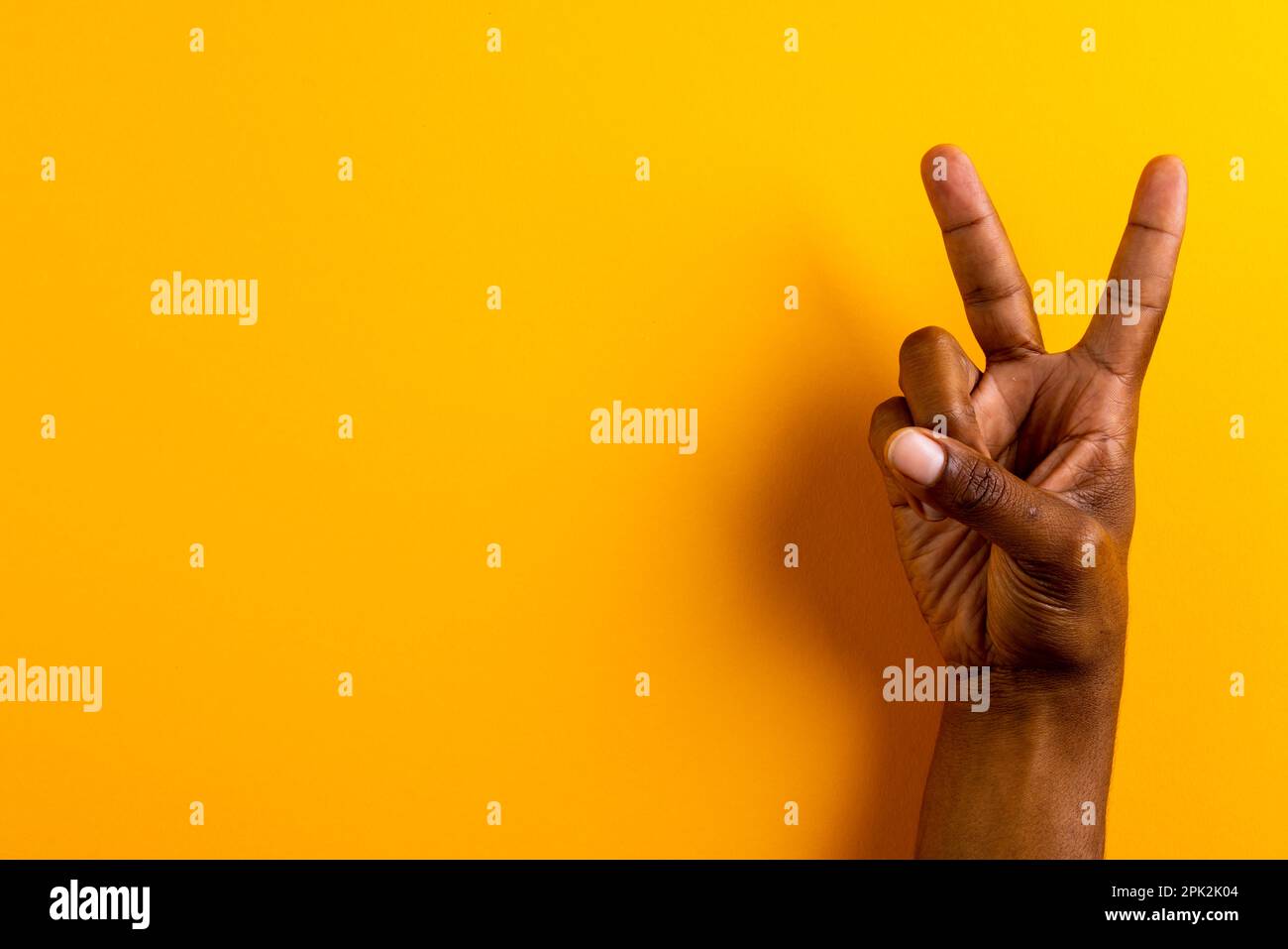 Gros plan de la main de l'homme biracial montrant le signe de paix avec l'espace de copie sur fond jaune Banque D'Images