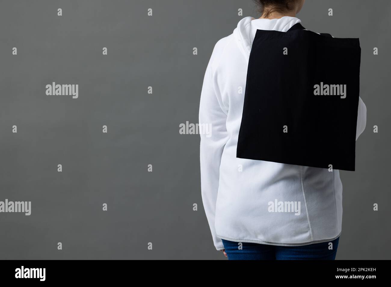Femme caucasienne tenant par-dessus l'épaule sac en toile noire avec espace pour copier sur fond gris Banque D'Images