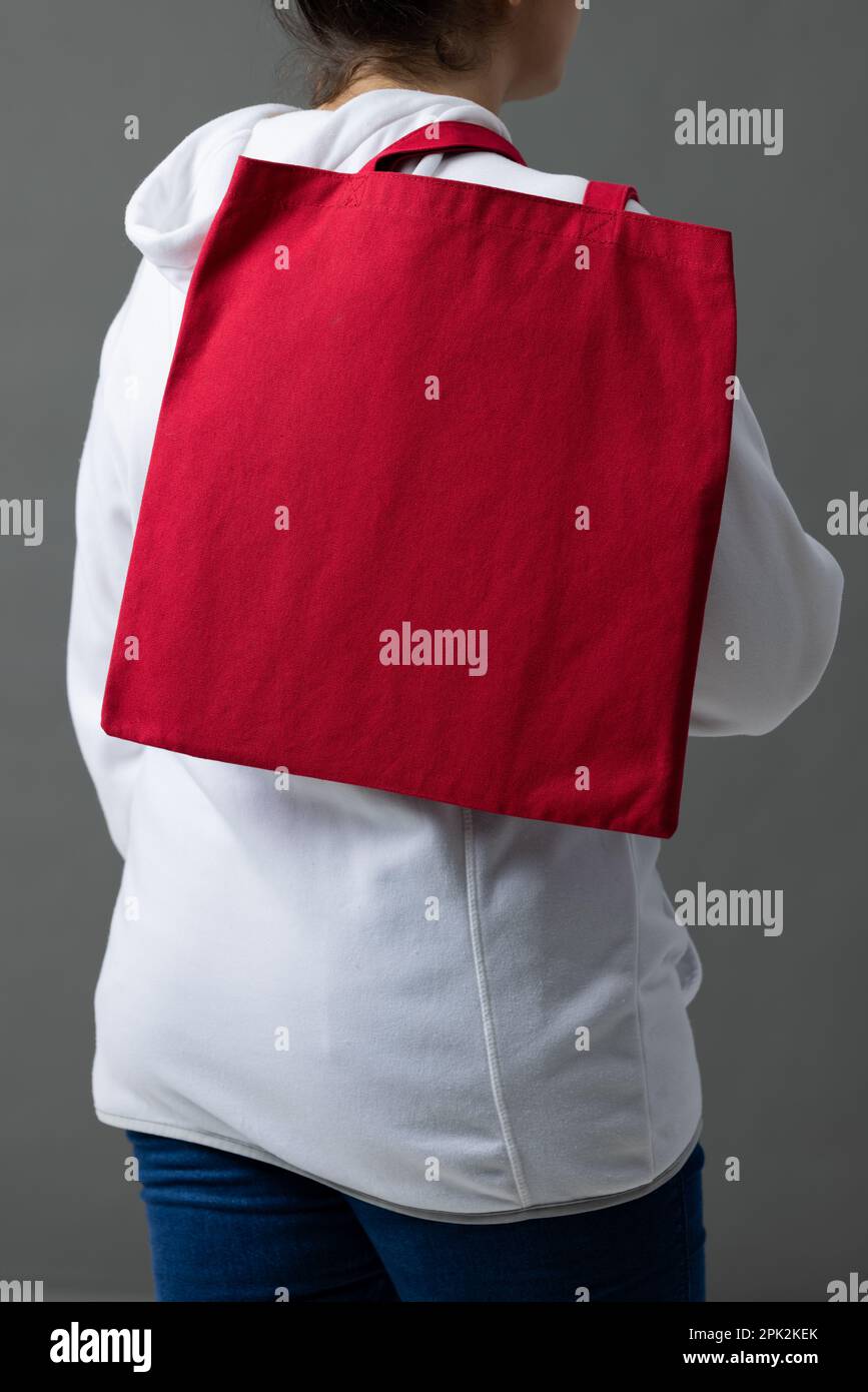 Femme caucasienne tenant par-dessus l'épaule sac en toile rouge avec espace de copie sur fond gris Banque D'Images