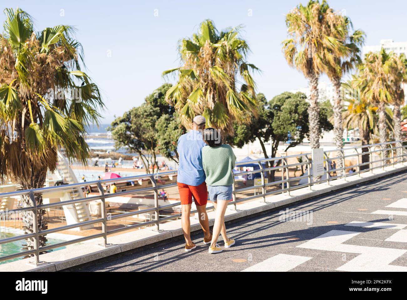 Couple divers tenant les mains et marchant le long de la promenade au bord de la mer Banque D'Images