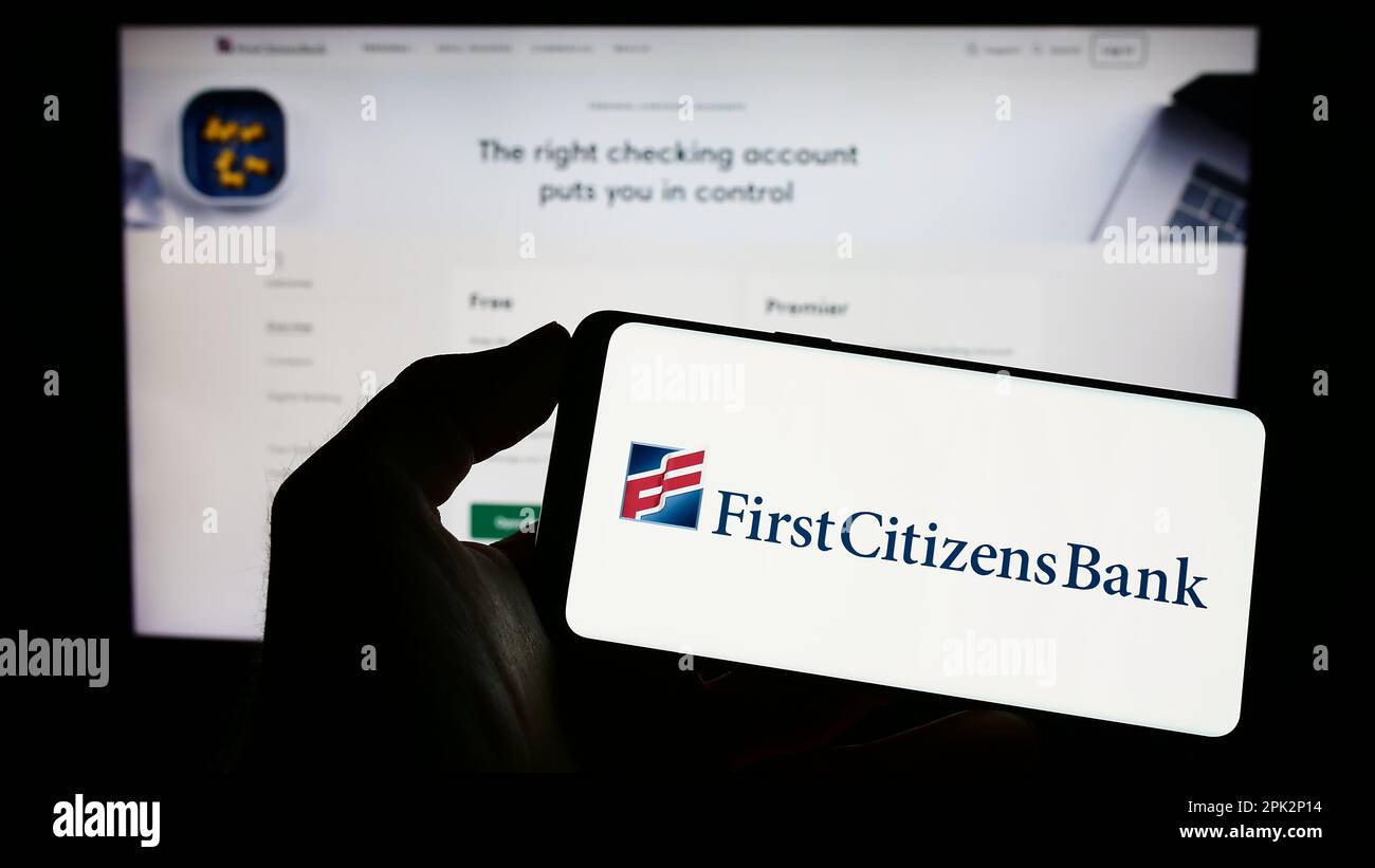 Personne tenant un téléphone portable avec le logo de la société financière américaine First Citizens Bank à l'écran en face de la page Web d'affaires. Mise au point sur l'affichage du téléphone. Banque D'Images