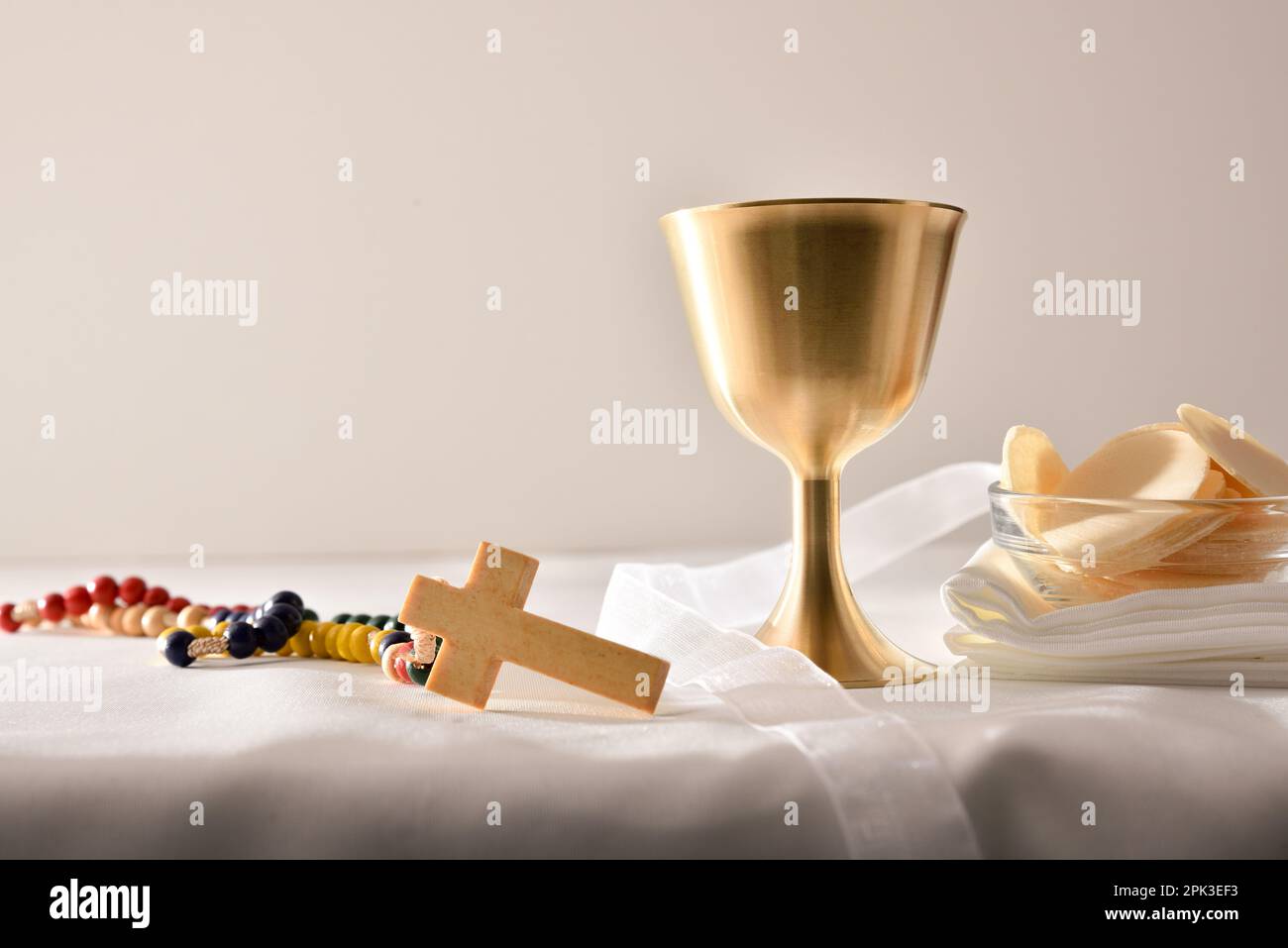 Coupe de calice au vin et hôtes consacrés dans un récipient sur table avec nappe et croix chrétienne en bois et fond blanc isolé. Vue avant Banque D'Images