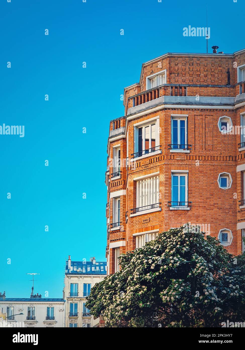 Magnifique bâtiment en brique orange avec un arbre en fleur au fond d'un ciel bleu clair à Asnieres-sur-seine, une banlieue de Paris, en France Banque D'Images