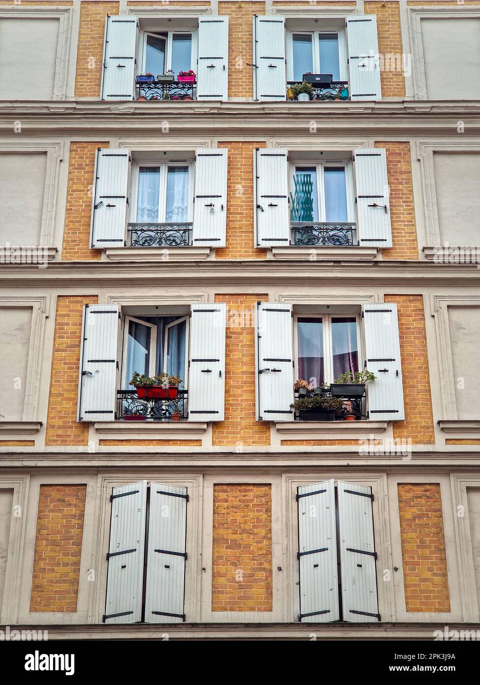 Façade de bâtiment avec murs de maçonnerie en briques peints en jaune et fenêtres avec persiennes extérieures blanches Banque D'Images