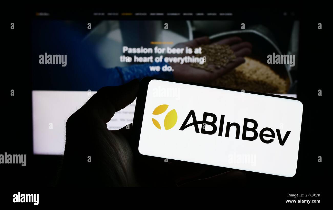 Personne tenant un téléphone portable avec le logo de la société de brassage Anheuser-Busch InBev (AB InBev) à l'écran en face de la page web. Mise au point sur l'affichage du téléphone. Banque D'Images