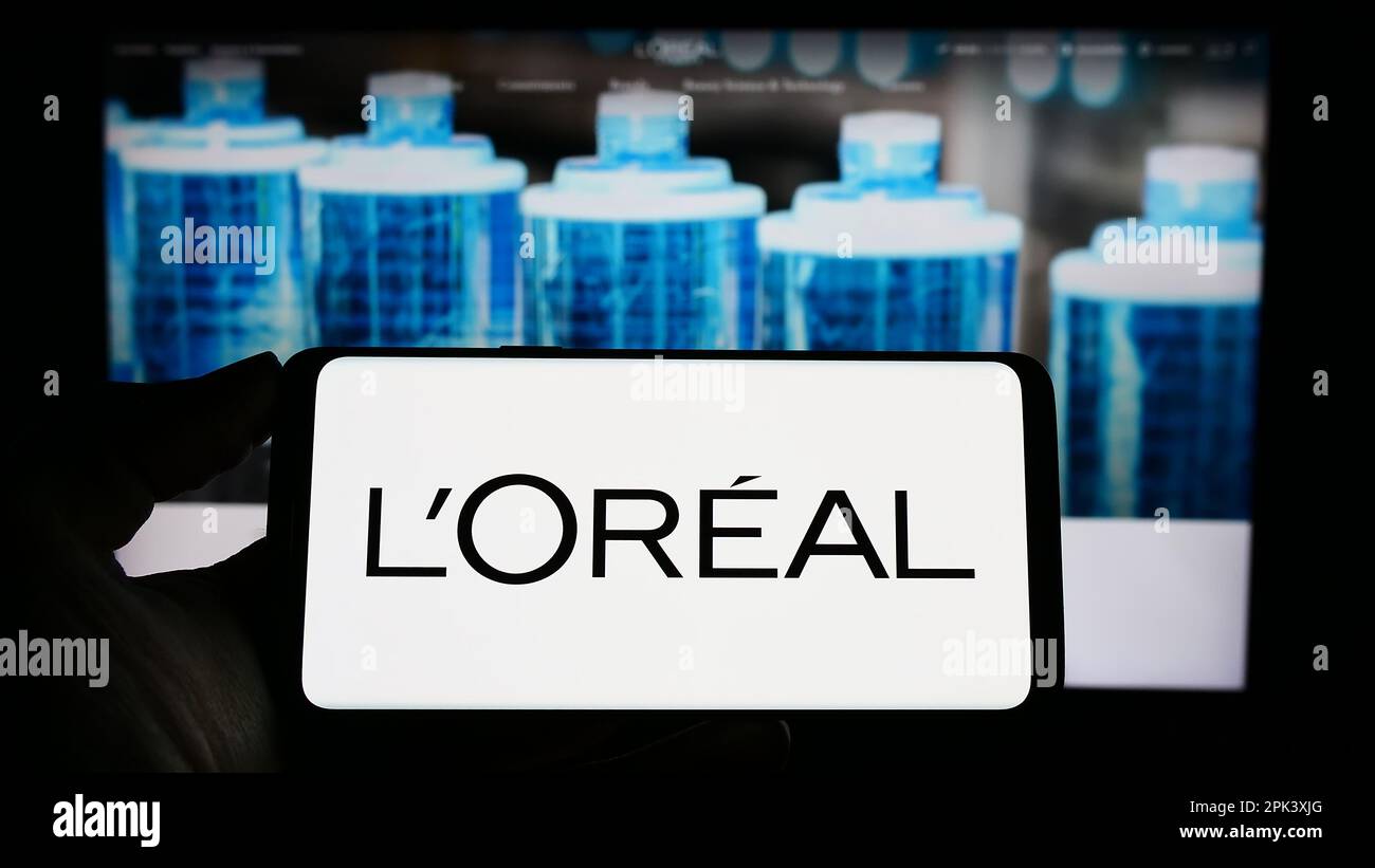 Personne tenant un smartphone avec le logo de la société française de soins personnels l'Oréal S.A. à l'écran devant le site Web. Mise au point sur l'affichage du téléphone. Banque D'Images
