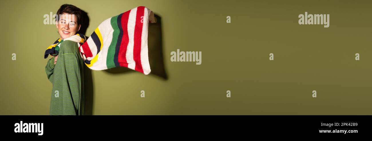 femme surjoyeuse dans un pull tendance et foulard rayé agitant sur le vent sur fond vert, bannière, image de stock Banque D'Images