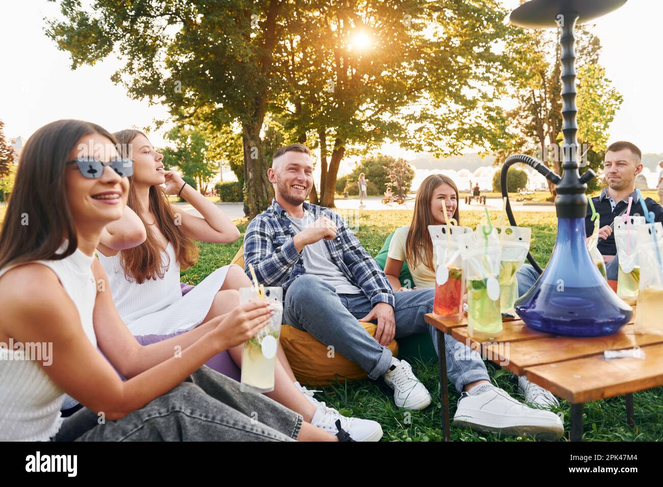 Asseyez-vous dans les sacs de fauteuil et fumer le nargua. Un groupe de jeunes ont une fête dans le parc pendant la journée d'été Banque D'Images