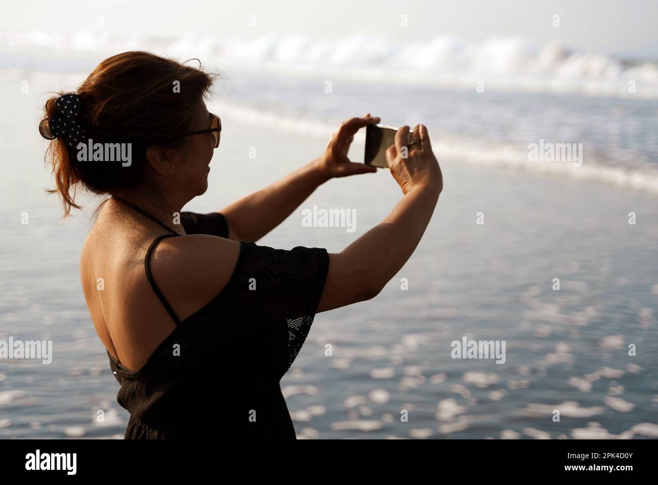 Femme à la plage prenant des photos des vagues de l'océan avec son téléphone. Concept de voyage et de vacances. Banque D'Images