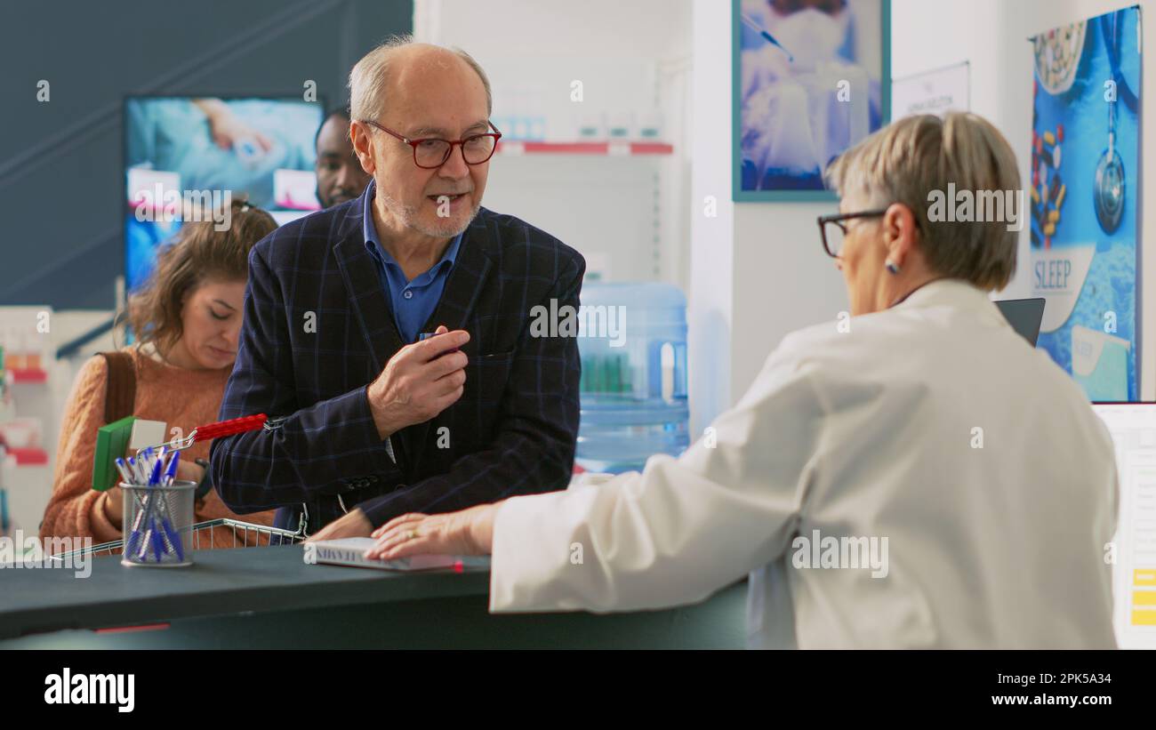 Client senior mettant des boîtes de médicaments sur le comptoir de la pharmacie, achetant des pilules et des suppléments pour le traitement de la récription. Homme prenant des produits pharmaceutiques dans un sac d'achats, caisse enregistreuse. Banque D'Images