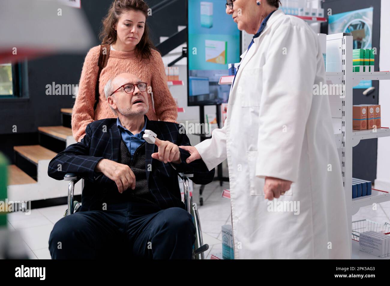 Utilisateur en fauteuil roulant parlant avec un employé de pharmacie de la  prescription tandis que le pharmacien mesure la température à l'aide d'un  thermomètre en pharmacie. Employé aidant le client avec le
